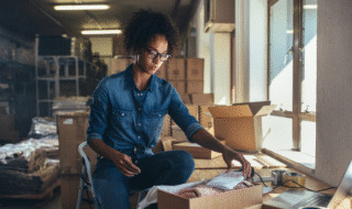African American female sitting on a stool in a workshop by a window during the day filling and online order