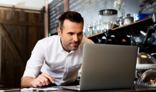 A restaurant owner working on his computer while wearing a white smock