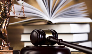 Photo of a judge's mallet beside law books and a state of the scales of justice