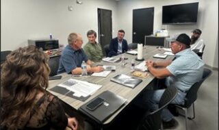 Six professionals sit around a conference table reviewing documents in a modern meeting room.
