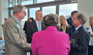 Group of professionally dressed adults chatting at a daytime networking event near glass doors in a bright lobby.