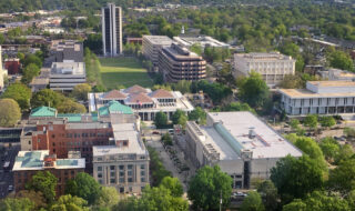Aerial view of a university campus with a green quad, surrounding buildings, and a tall white tower.
