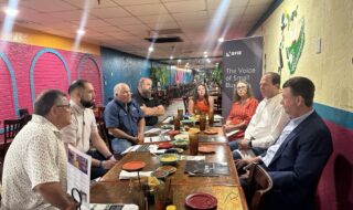 Group of nine adults seated around a long dining table in a colorful restaurant, NFIB banner reads 'The Voice of Small Business' in the background.