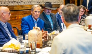Group of professionals at a dinner meeting around a long table in a rustic restaurant; a man in a blue blazer speaks.