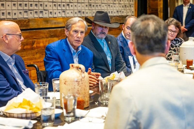 abbott - NFIB Group of professionals at a dinner meeting around a long table in a rustic restaurant; a man in a blue blazer speaks.